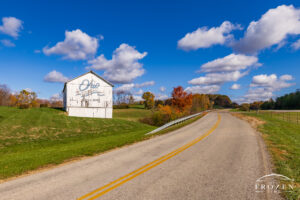 An old white barn as its stands among the rolling hills of Athens County displaying the Ohio Bicentennial logo where the paint is fading after 25 years of wear.