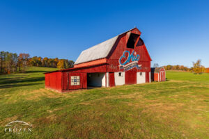 A gorgeous red barn displaying a blue version of the Ohio Bicentennial logo on an autumn evening where the warm light paints the barn in surrounding hillside in perfect light.