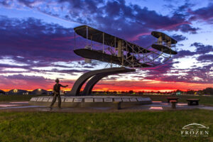 1909 Wright Flyer during Colorful Twilight No 46 | Art of Frozen Time 1909 Wright Flyer Memorial in Dayton Ohio with fiery sunset on the horizon and pink and purple clouds above the illuminated sculpture