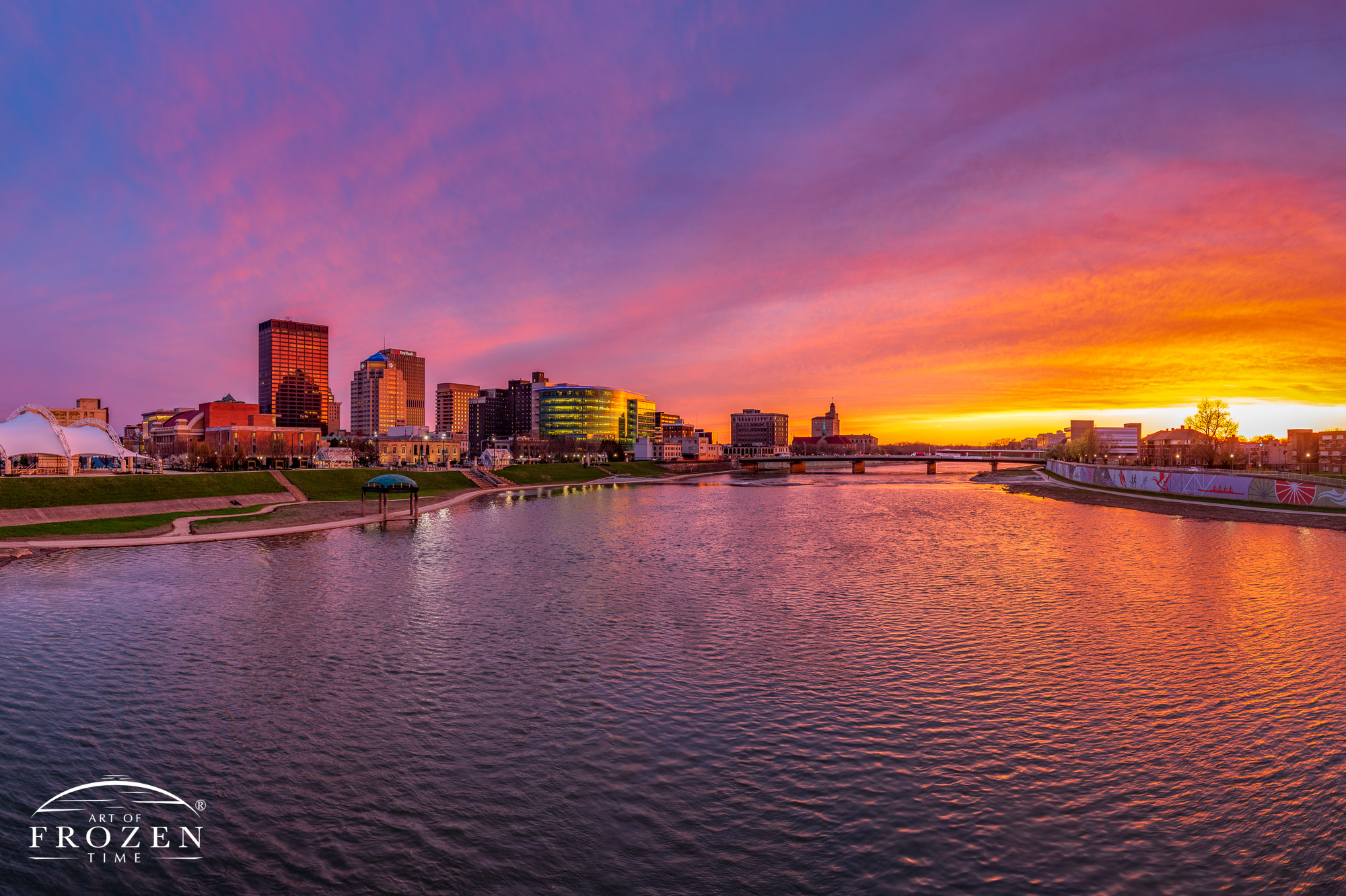 Colorful Dayton skyline sunset where the sun illuminated the clouds from underneath in warm colors as the Miami River took on interesting texture