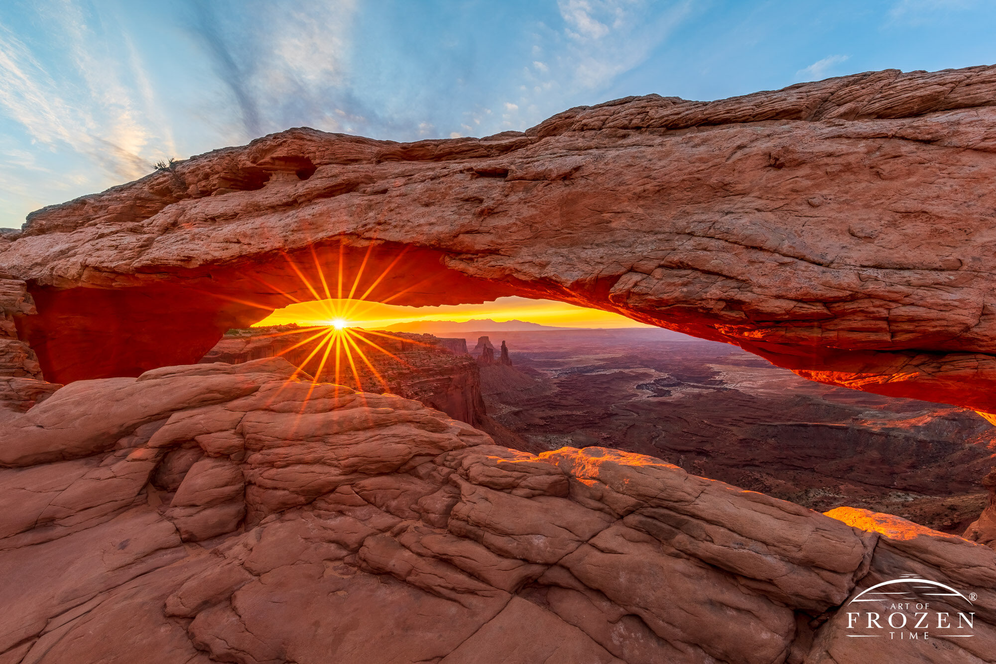 A sunrise as viewed through Mesa Arch where the warm orange colors paint the underside of the rock arch