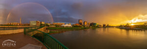Panorama of the Dayton Skyline where the sun peeks through a sliver of clear air at sunset which produces a full rainbow