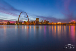 St Louis skyline during a colorful twilight where distant clouds refract red hues as the city lights begin to make the skyline glow.