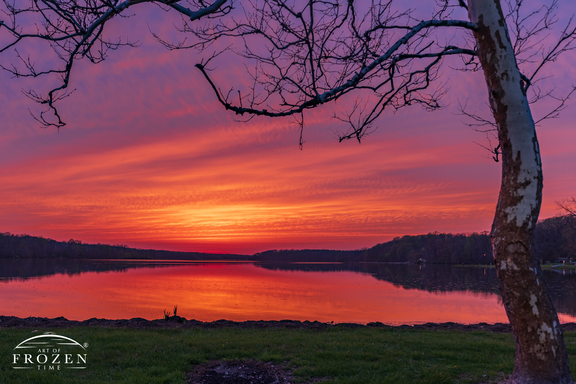 A cloud-filled sunset turns colorful as twilight deepens over Kiser Lake where the calm waters reflect the sky above.