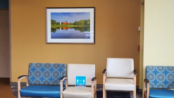 A large nostalgic print of a red barn and silo by a pond in the waiting room of the Primary Care Beaver View Health Center