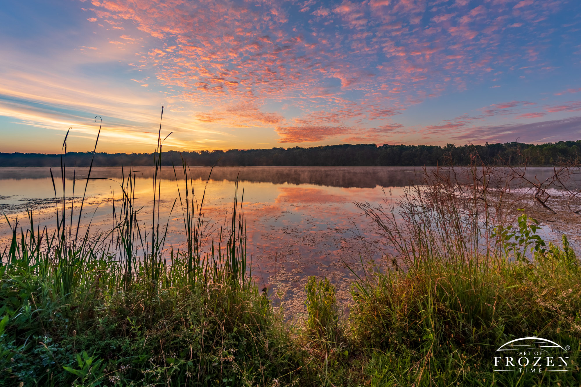 A colorful sunrise over Spring Valley Wildlife Area where various cloud layers color the scene in their own way and the still lake waters form a mirror reflection