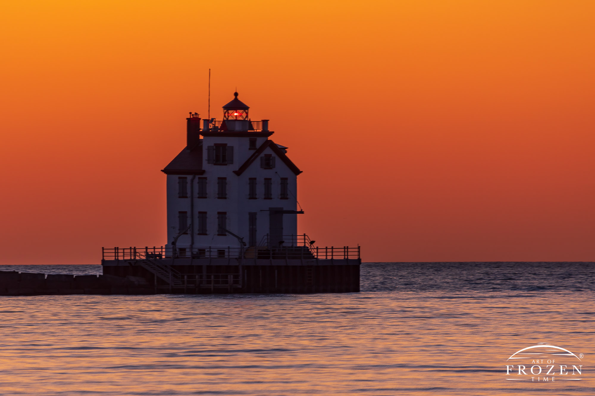 Twilight over Lorain Lighthouse as the clear Lake Erie horizon takes on varying orange hues while the lake surface refracts light from the darker blue skies above.