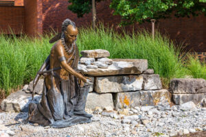 A bronze sculpture a Native American kneeling by a water source
