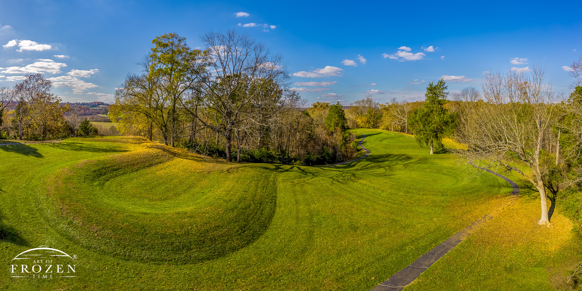 Ohio’s famous Serpent Mound from an elevated vantage point as autumn leaves selectively color the terrain features under blue skies.