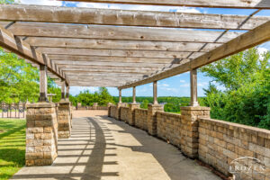 a view from under the covered platform at E. Milo Beck Park in Springboro Ohio where the rows of trellis beams leas the eye to the open plaza and sky
