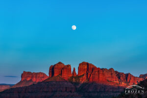 A full moon rising over Sedona’s Cathedral Rock where the setting sun paints the red sandstone in warm light creating a magical scene