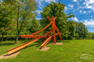 A bright orange sculpture of eight curved steel I-beams placed in a mix of horizontal and vertical positions