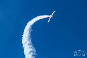 Aerobatic airplane flying vertical before leveling offer while leaving a bright white contrail in a clear blue sky