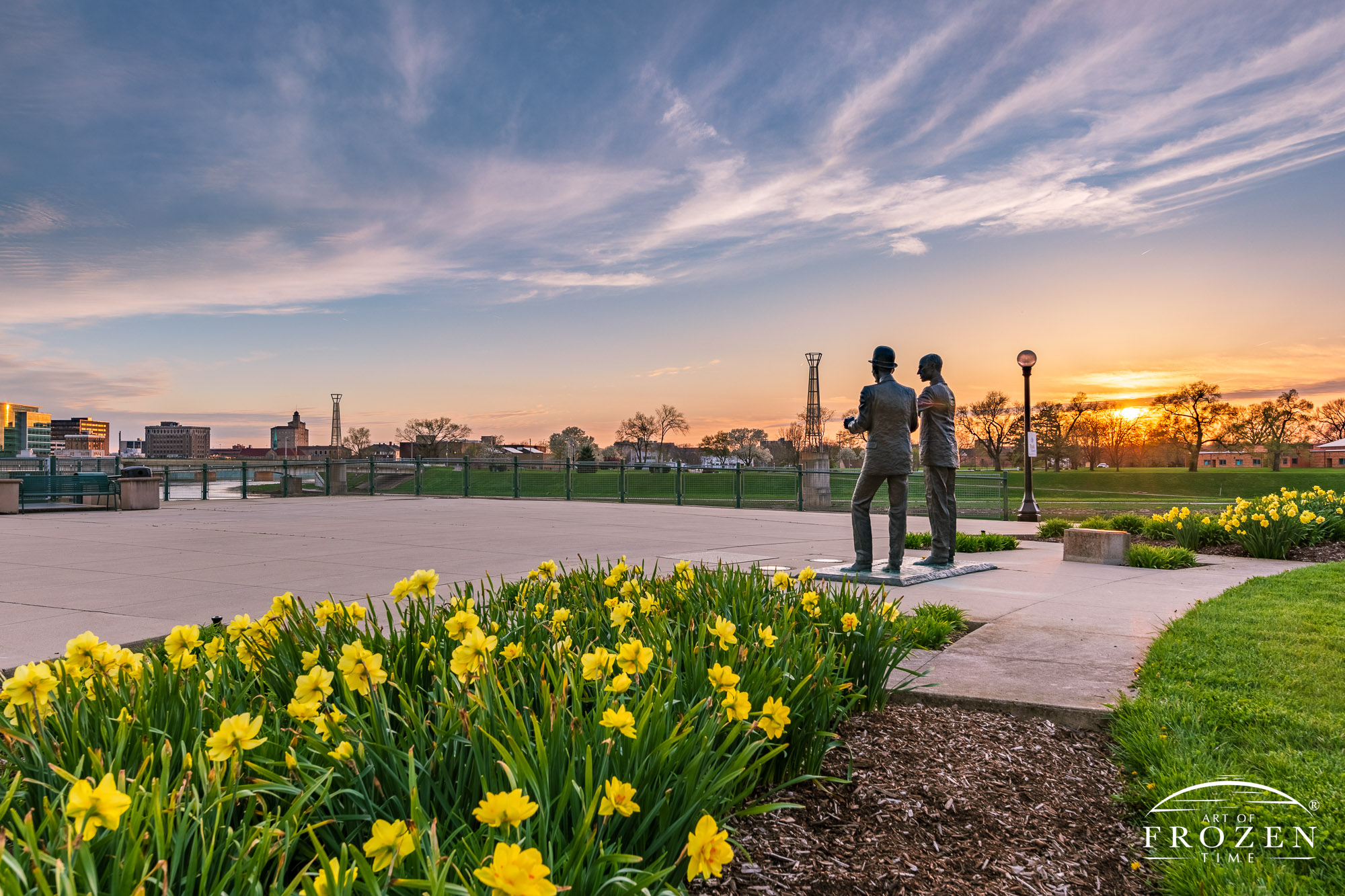 A bronze statue of Wilbur and Orville Wright overlooking the Dayton Skyline from Deeds Point during a spring sunset