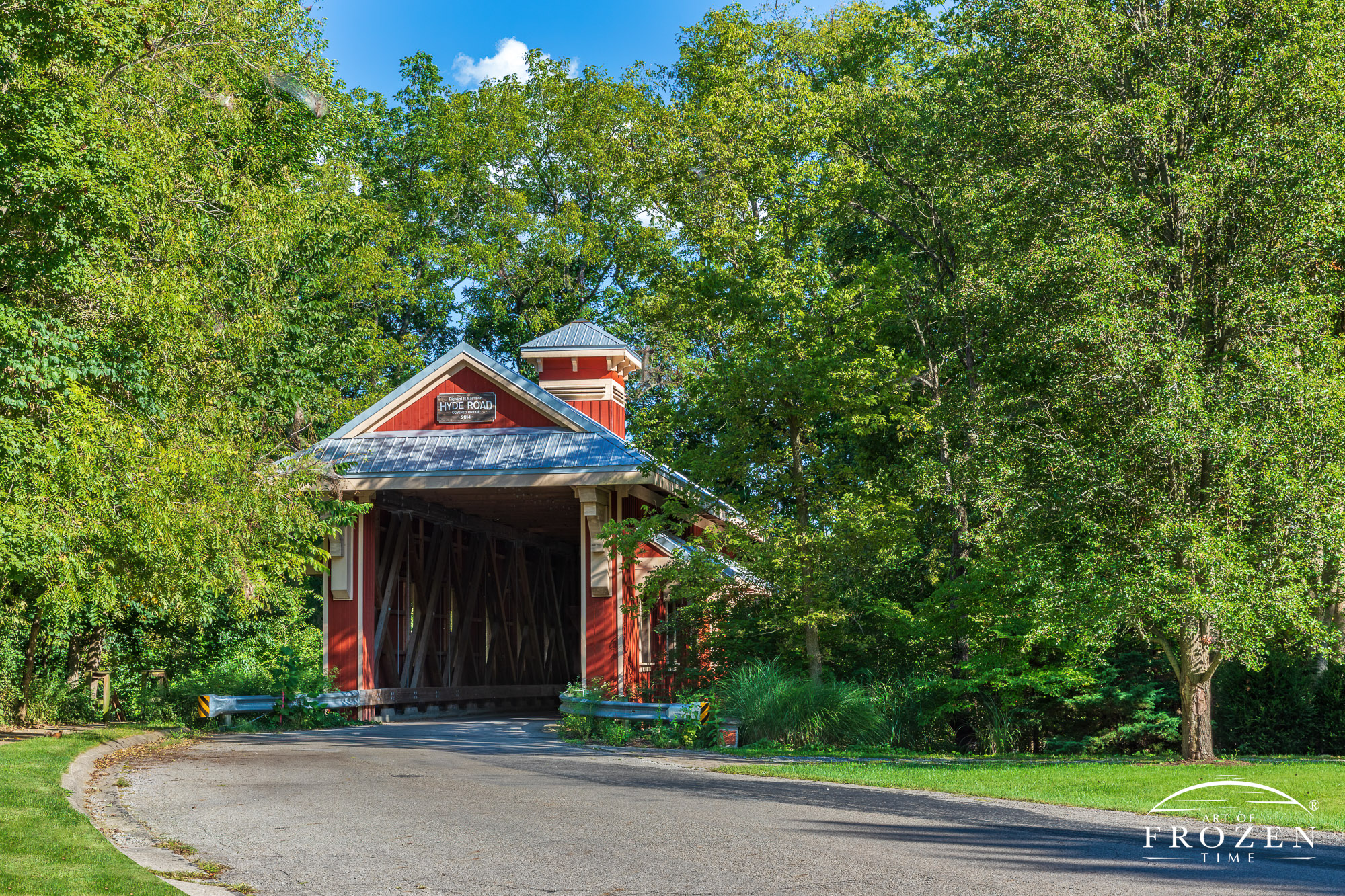 A bridge red covered bridge is surrounded by lush green trees under blue skies
