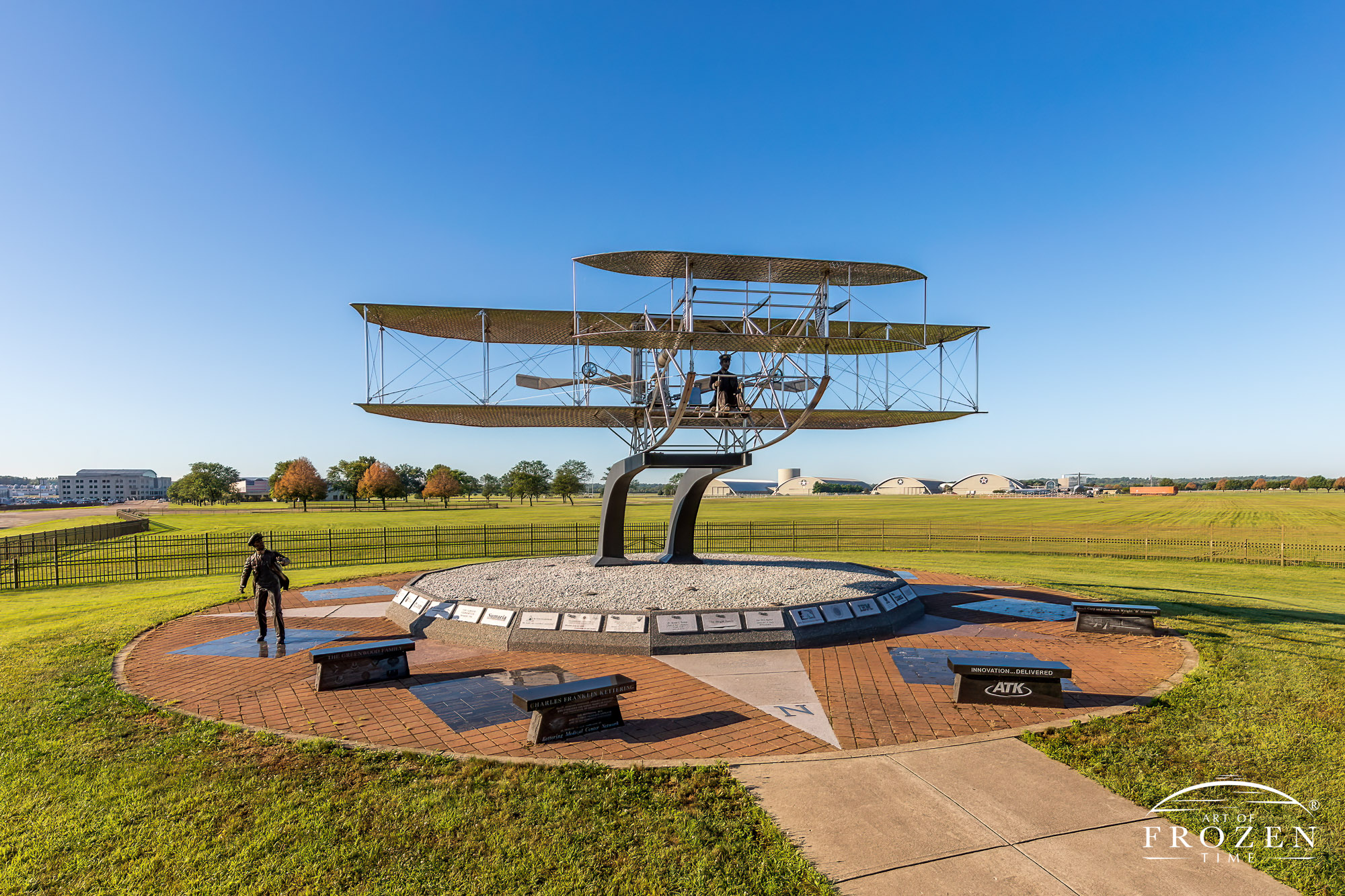 A replica of the 1909 Wright Flyer appears to have just taken flight outside WPAFB gate as morning golden lights shines on the sculpture