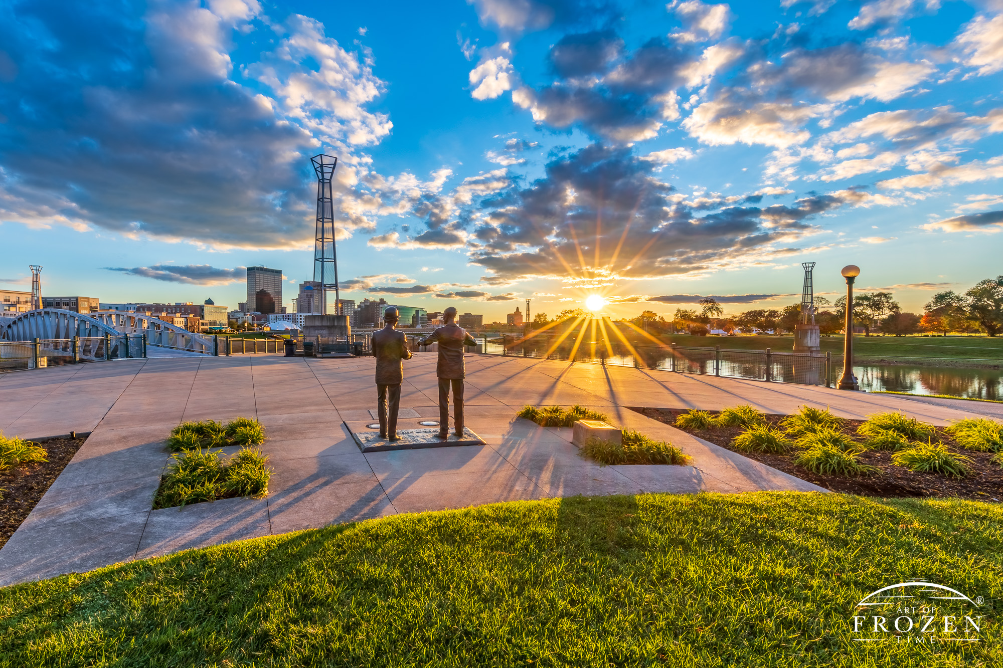 An autumn sunset over Dayton, Ohio where the foreground shows backlit sculptures of Wilbur and Orville Wright looking towards the setting sun rendered as a stunning starburst