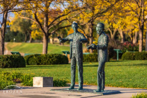 Statue of the Wright Brothers surround by trees taking on their autumn color in evening light