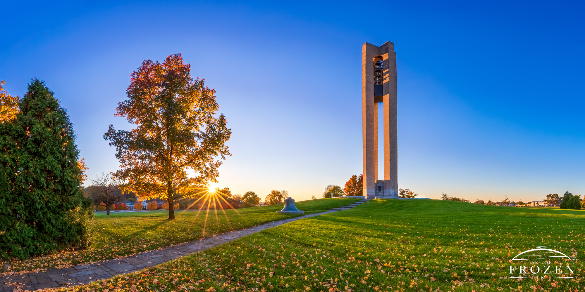 An autumn sunset painting Dayton’s Deeds Carillon in golden light as rays rake across the green grass and fall leaves