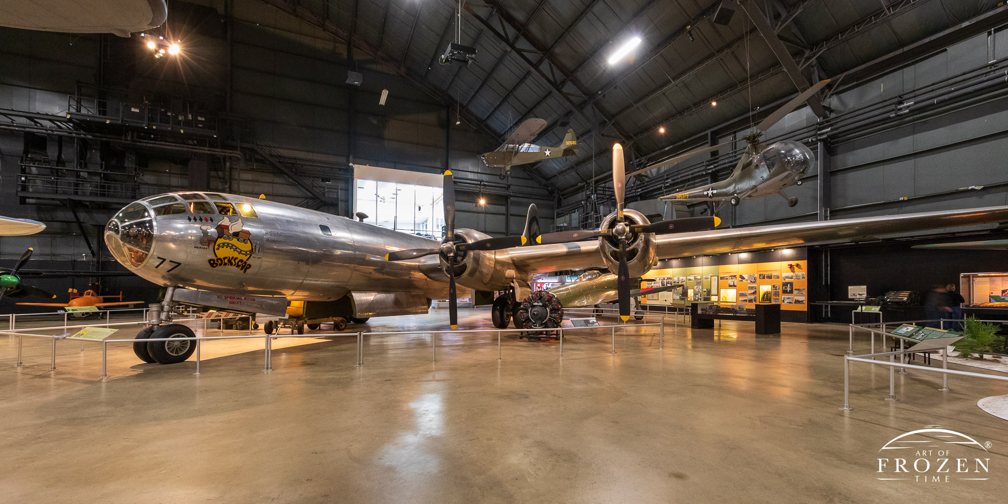 A panoramic view of a B-29 Bomber featuring its bare aluminum skin and classic nose art as it sits inside the National Museum of the US Air Force