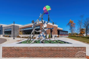 A stainless steel sculpture called Celebration lies in Cornerstone Park, Centerville Ohio as a stained glass ornament being held in the air by a stylized family dancing in a circle.