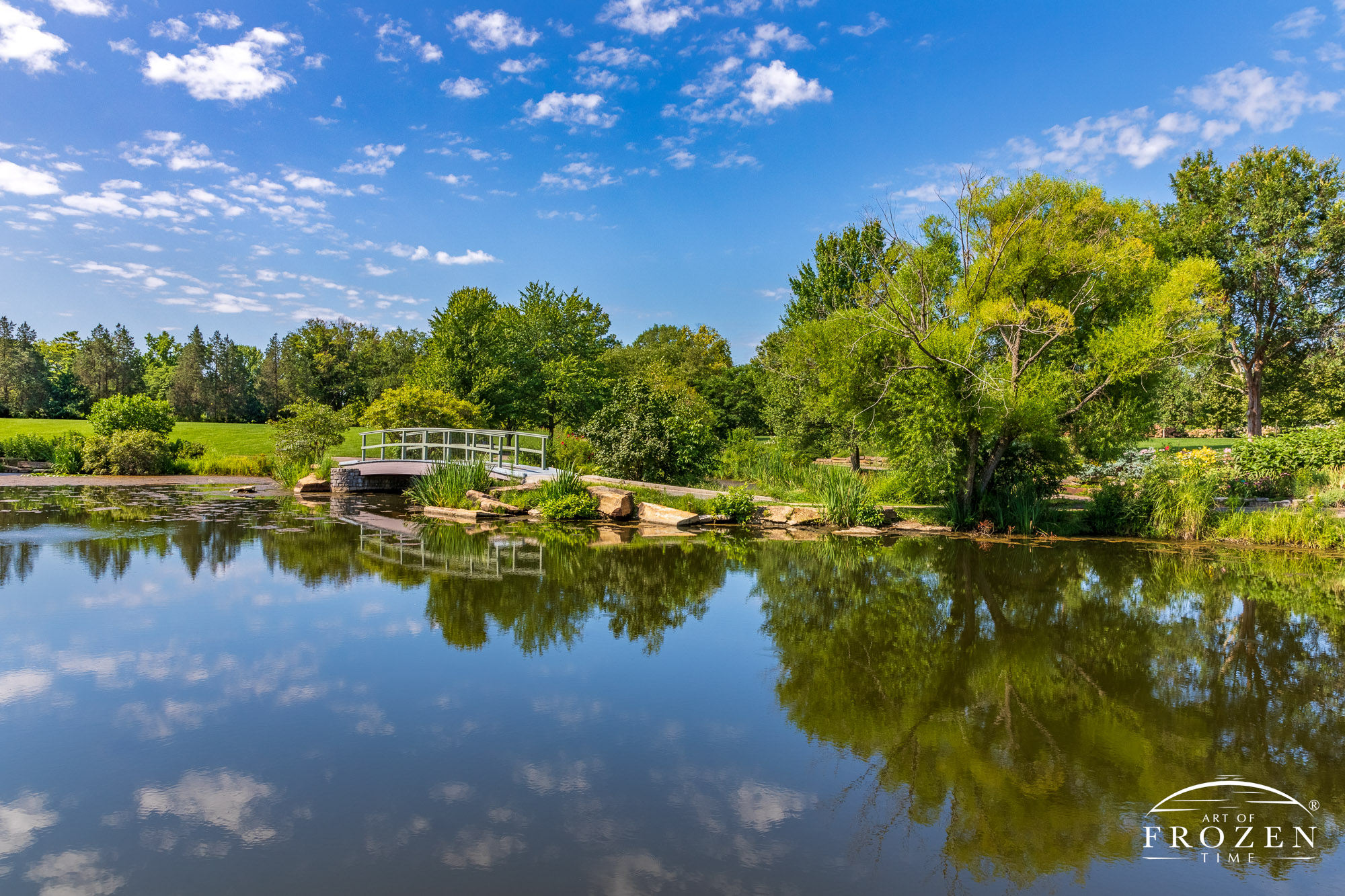 The Money Bridge and surround gardens reflected by the smooth waters of the Cox Arboretum Pond on a pretty day