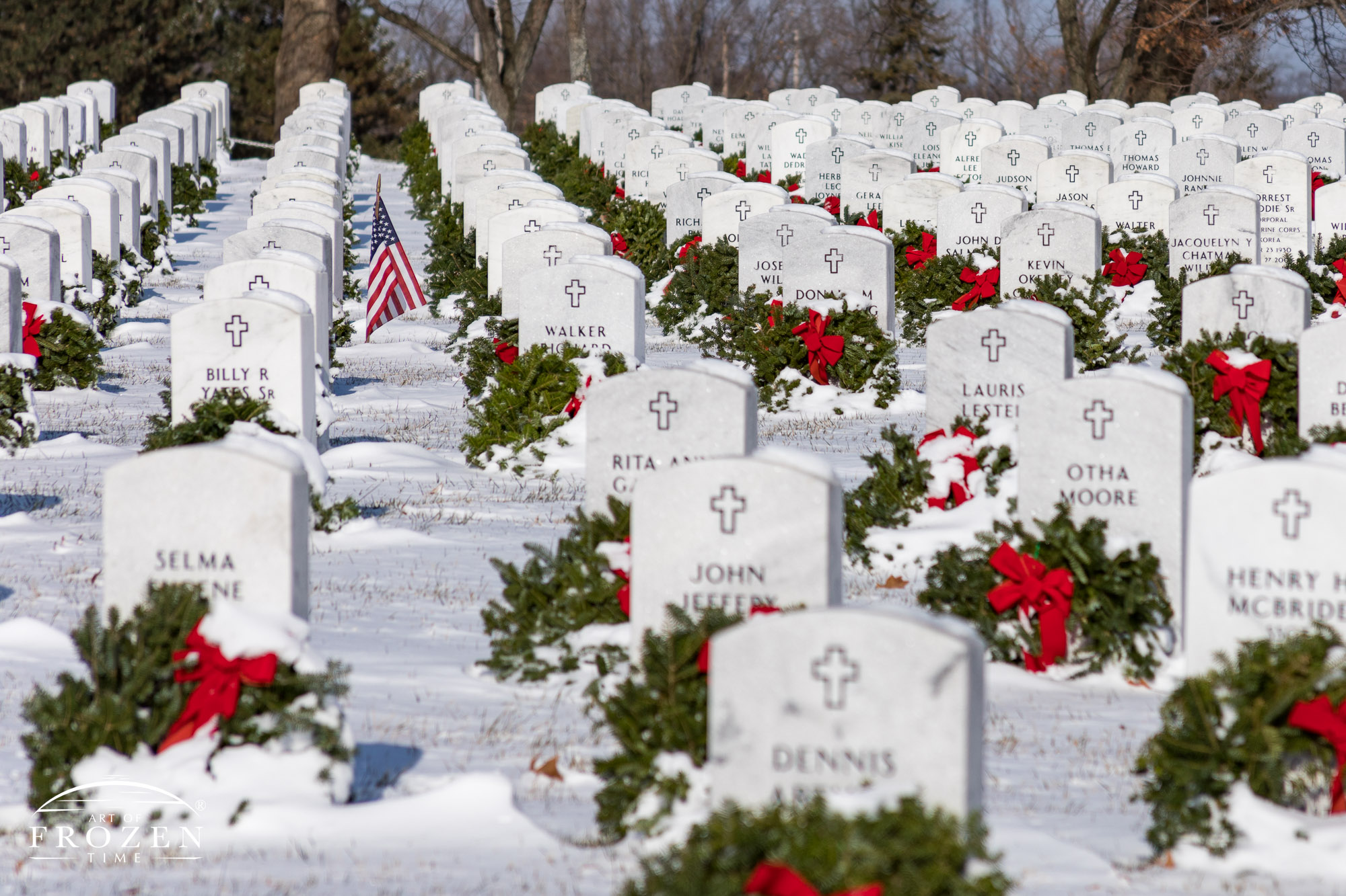 A patriotic image featuring orderly rows of white military headstones with each marker having its own green wreath and red ribbon, all covered in a fresh blank of snow on Christmas morning