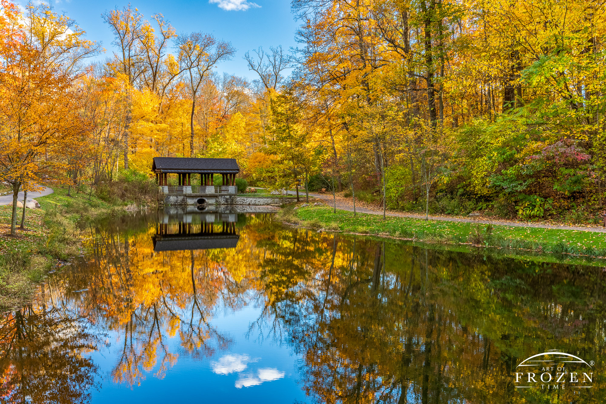 An Adirondack-style pavilion nested among bright yellow sugar maple trees and the calm pond perfectly reflects the entire scene