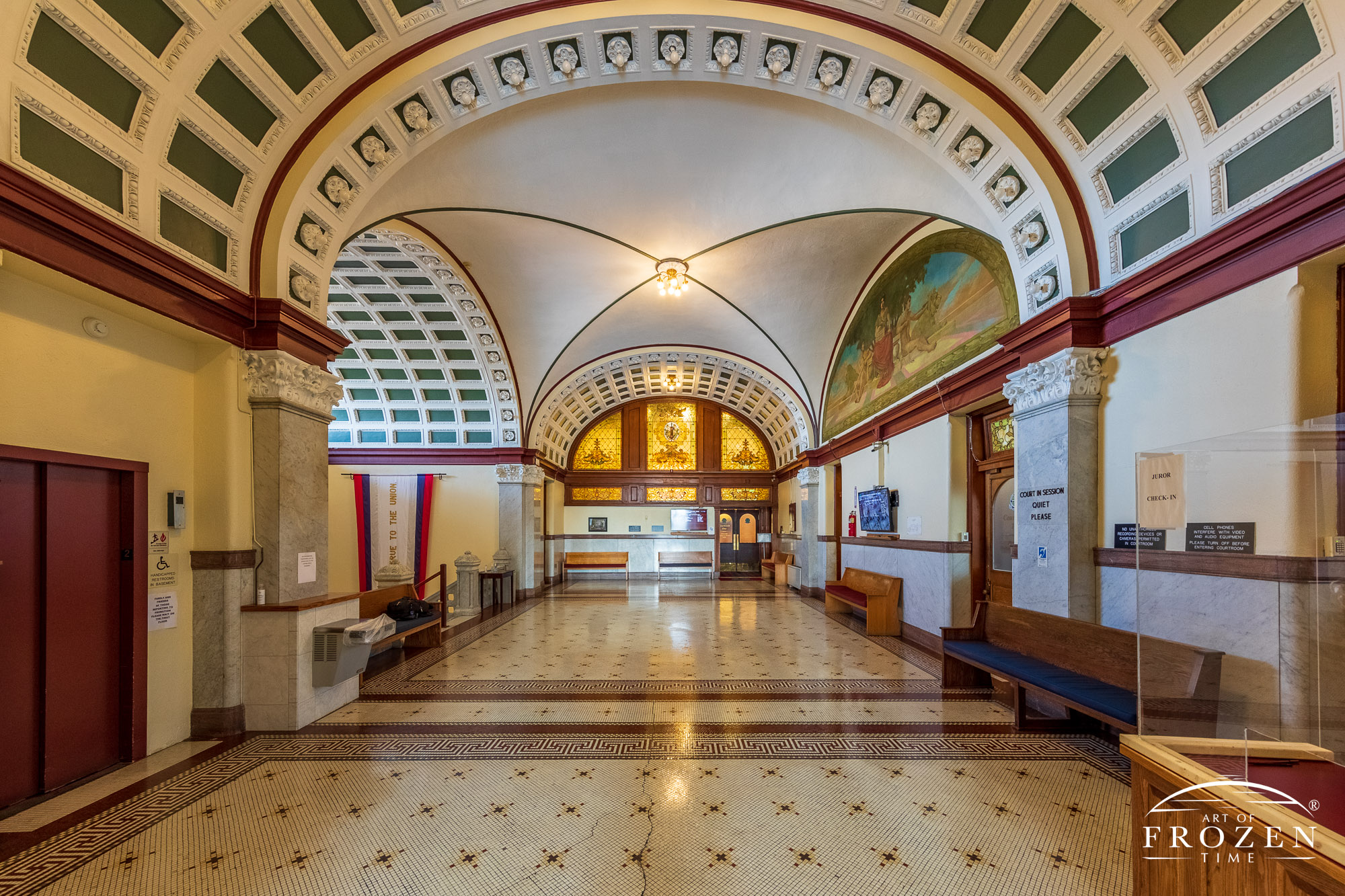 A courtroom hallway featuring vaulted ceilings, murals and stained glass windows