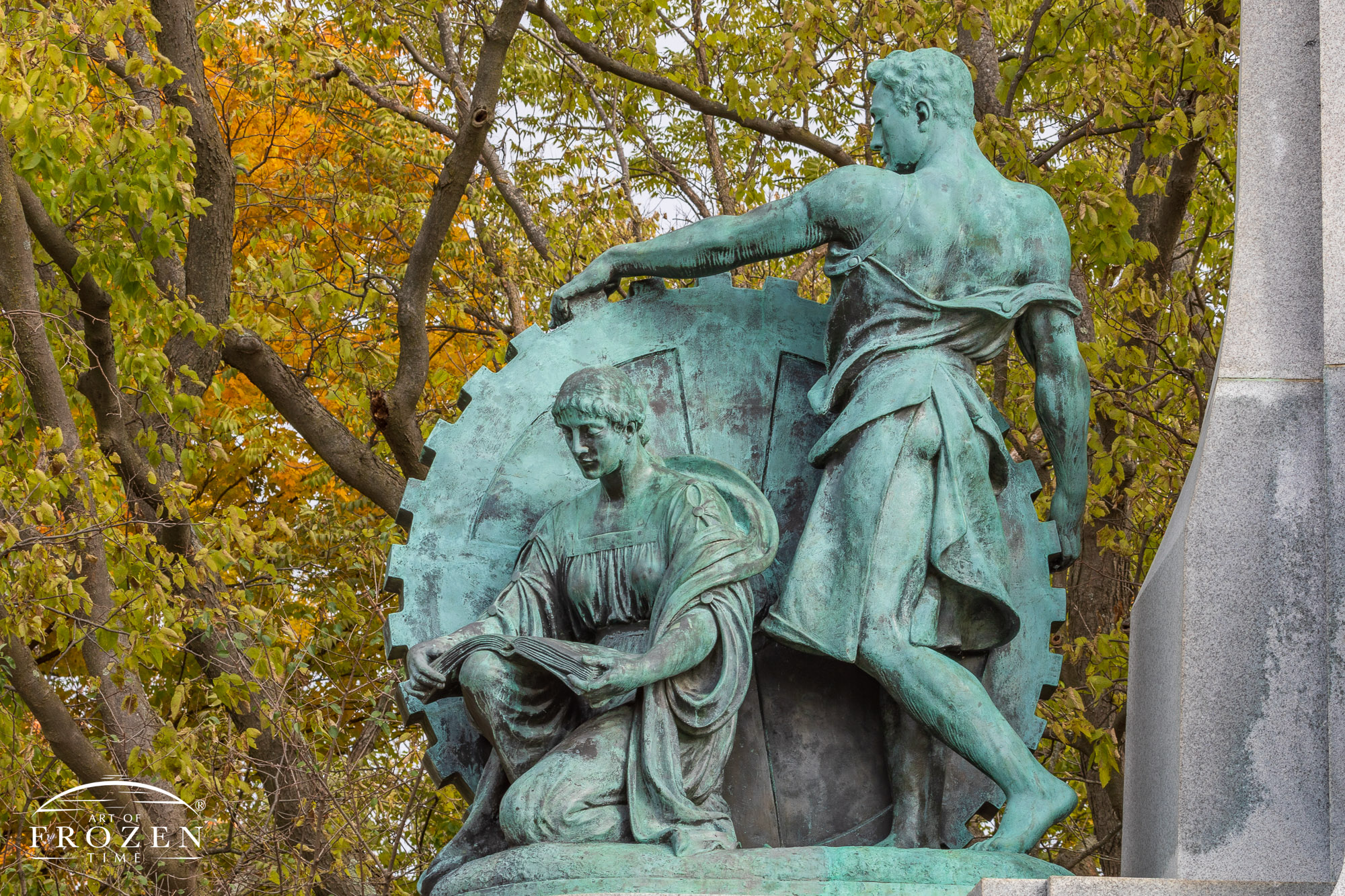 A bronze subgroup of John H. Patterson’s Memorial depicting a sculpture of a man maneuvering a large gear while a woman kneels next to him reading a book symbolizing his industrial and educational pursuits.