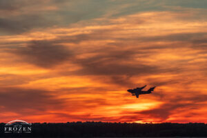 A shilloutte of a Boeing C-17 flying at sunset where high-level clouds take on evening's golden hues