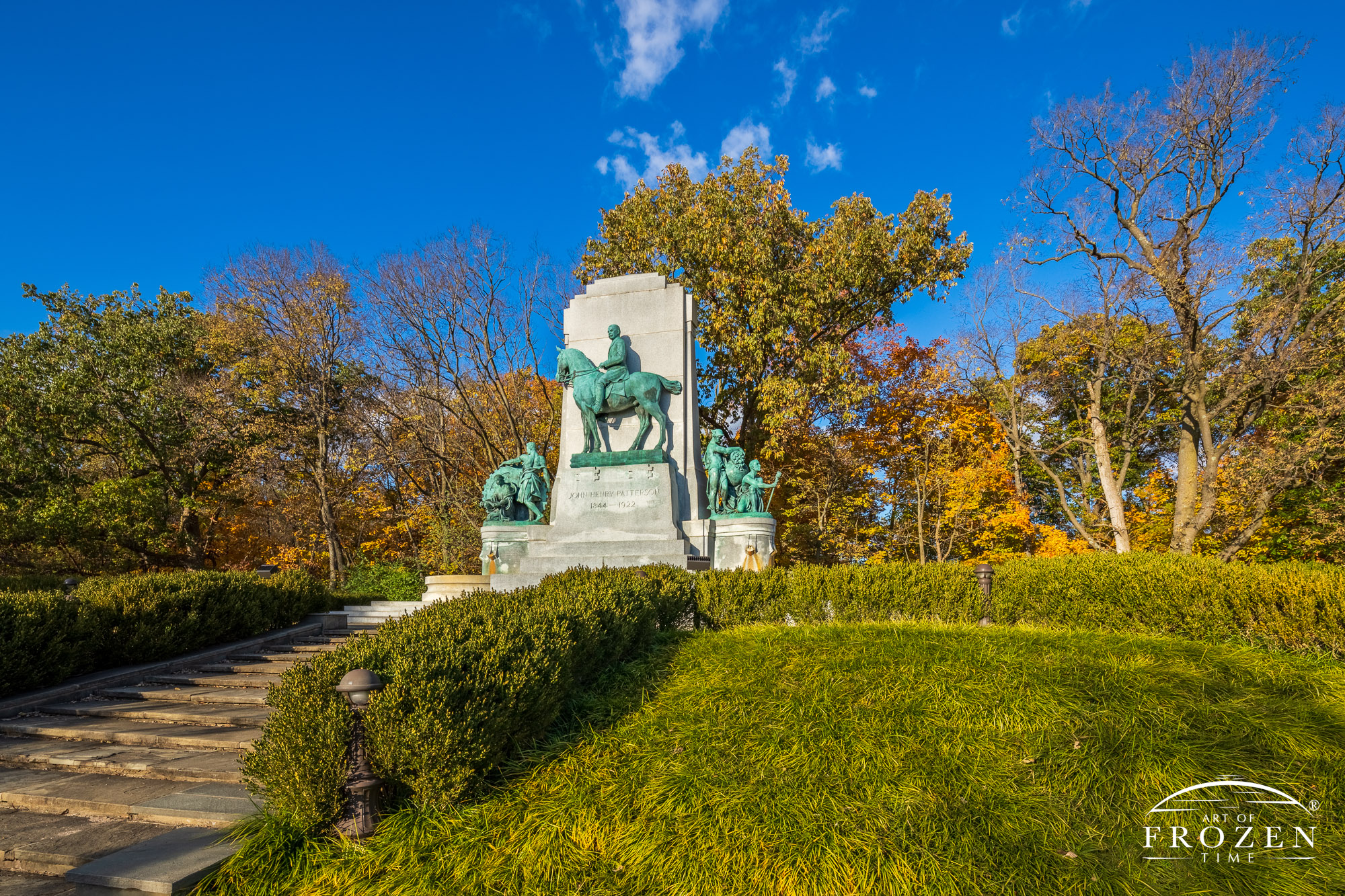 A equestrian style memorial for John H. Patterson stands under blue skies on a hill surrounded by autumn-colored trees