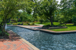A peaceful park scene where brick pathways form leading lines around flowing pools of water and perfectly landscaped gardens