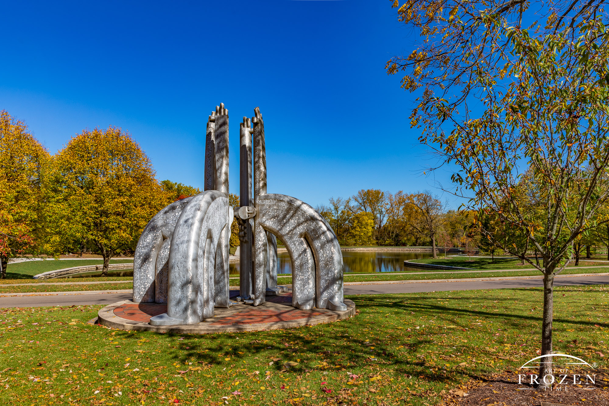 A fanciful sculpture in Lincoln Park which features aluminized people with outstreched arms which stretch from the ground towards the blue sky during an early fall day