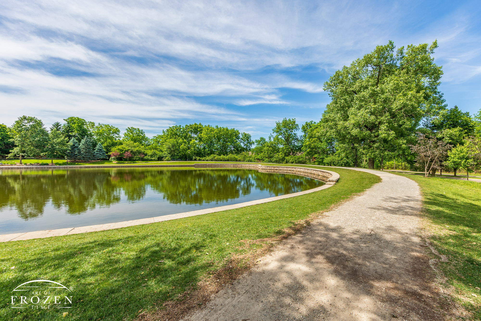 A walking path extends around a landscaped pond as cirrus clouds float overhead