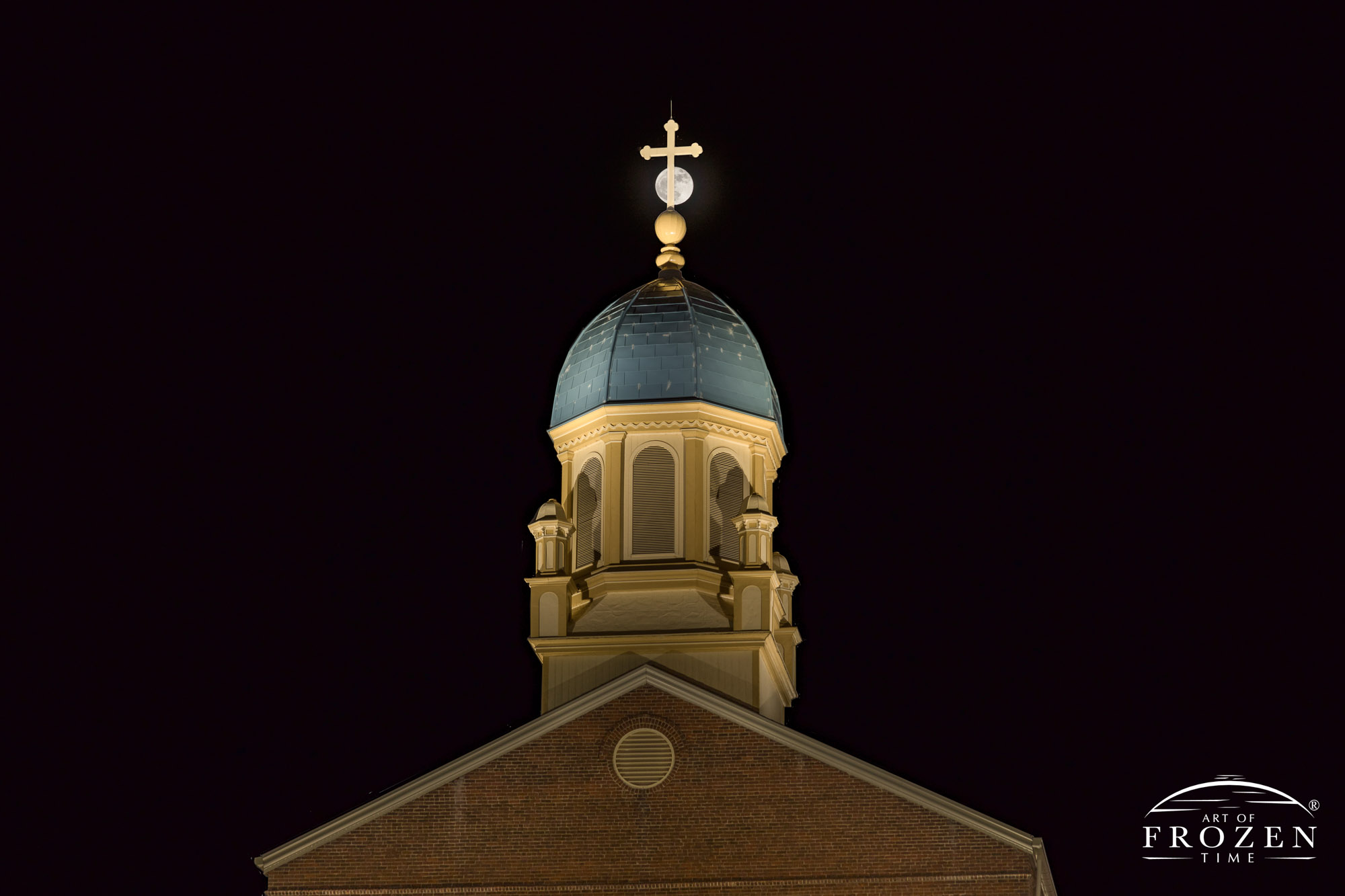 An intimate view of a moonrise over University of Dayton Chapel of the Immaculate Conception where the bell tower's crucifix stands in front of the moon