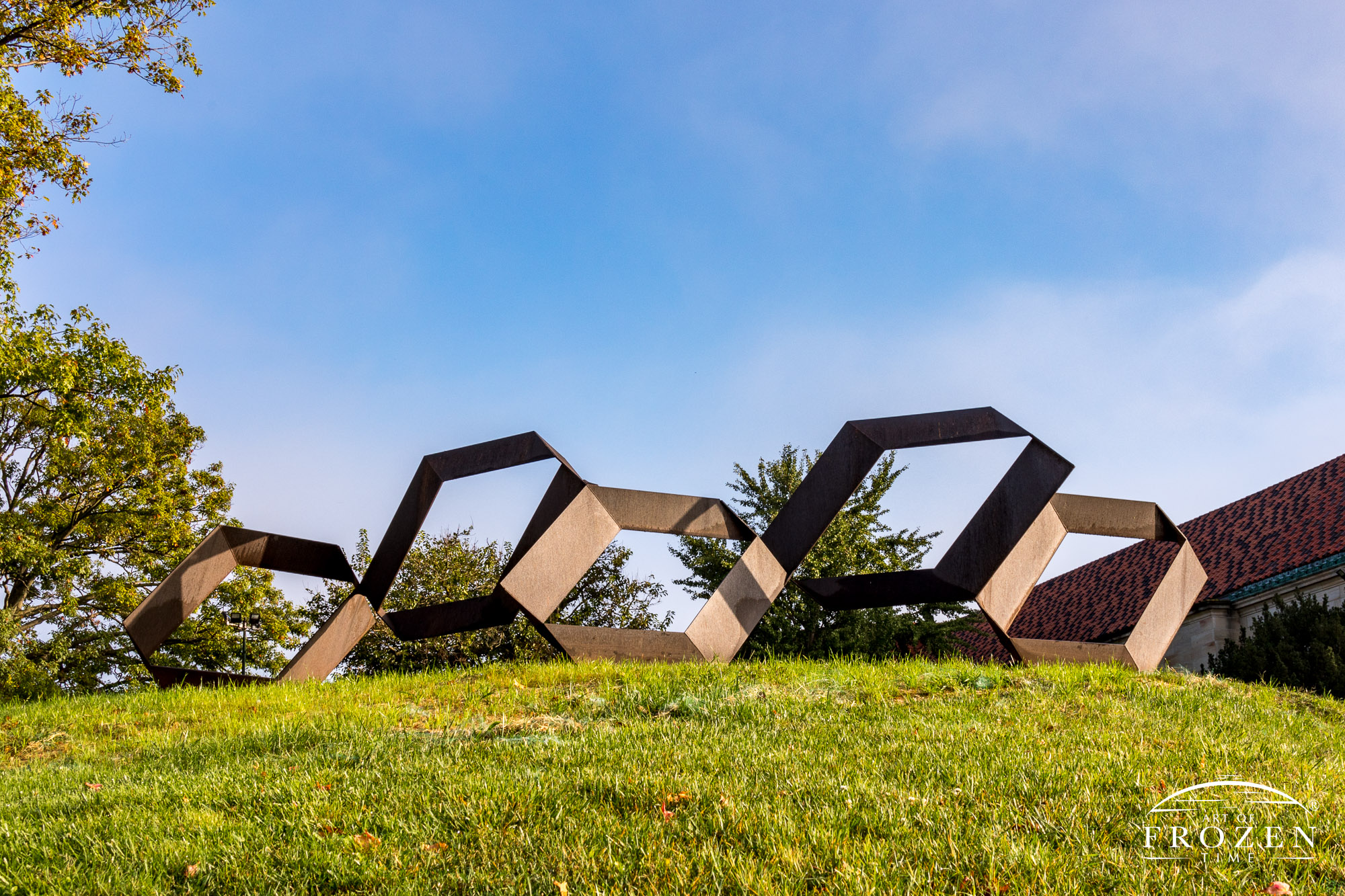 A sculpture resides on a small knoll consisting of abstract Olympic Rings in quadrilateral form while basking in the morning sun