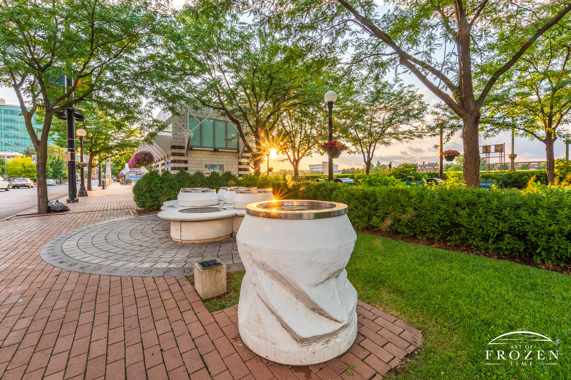 A sunset scene paying tribute to the inventor of the pop top can by a sculpture of a six pack of cans where the warm sunlight glints off the top of the display