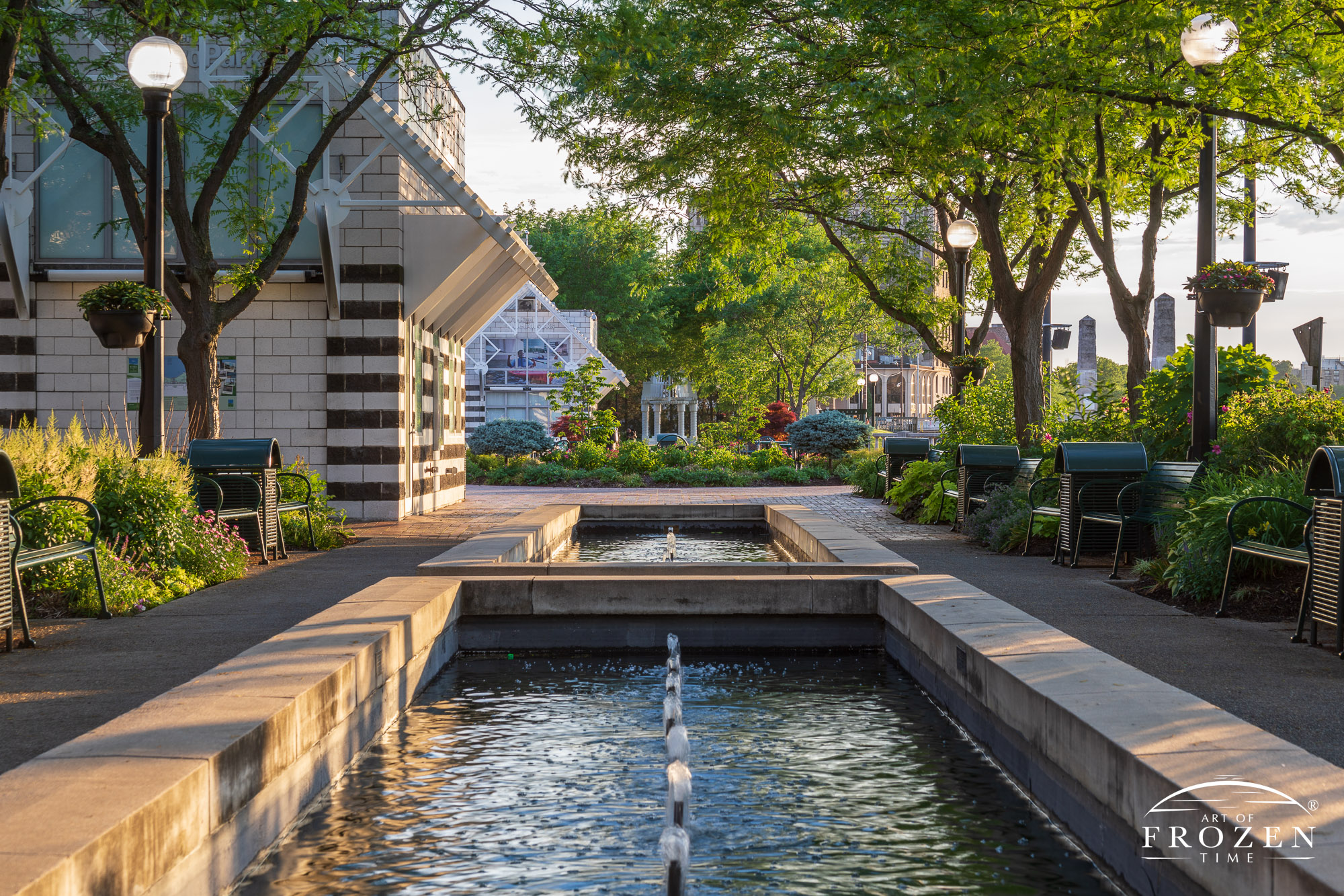 A cityscape scene from Dayton’s RiverScape MetroPark which long fountains offer trickle sounds as the setting sun washes the plaza in golden light.