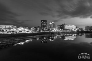 A black and white twilight image of the Dayton Skyline where the city lights become prominent and RiverScape’s lights complement the deepening twilight sky