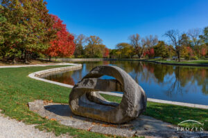 A rock sculpture at Kettering Civic Commons where the sunlight washes over the various cuts and surrounding trees transition to brilliant fall colors, all under a blue sky