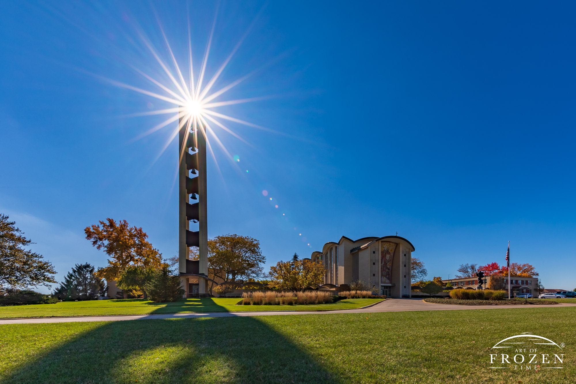 The sun forms a starburst which shines through the top of St Leonard Bell Tower which contrasts brightly against the blue fall skies