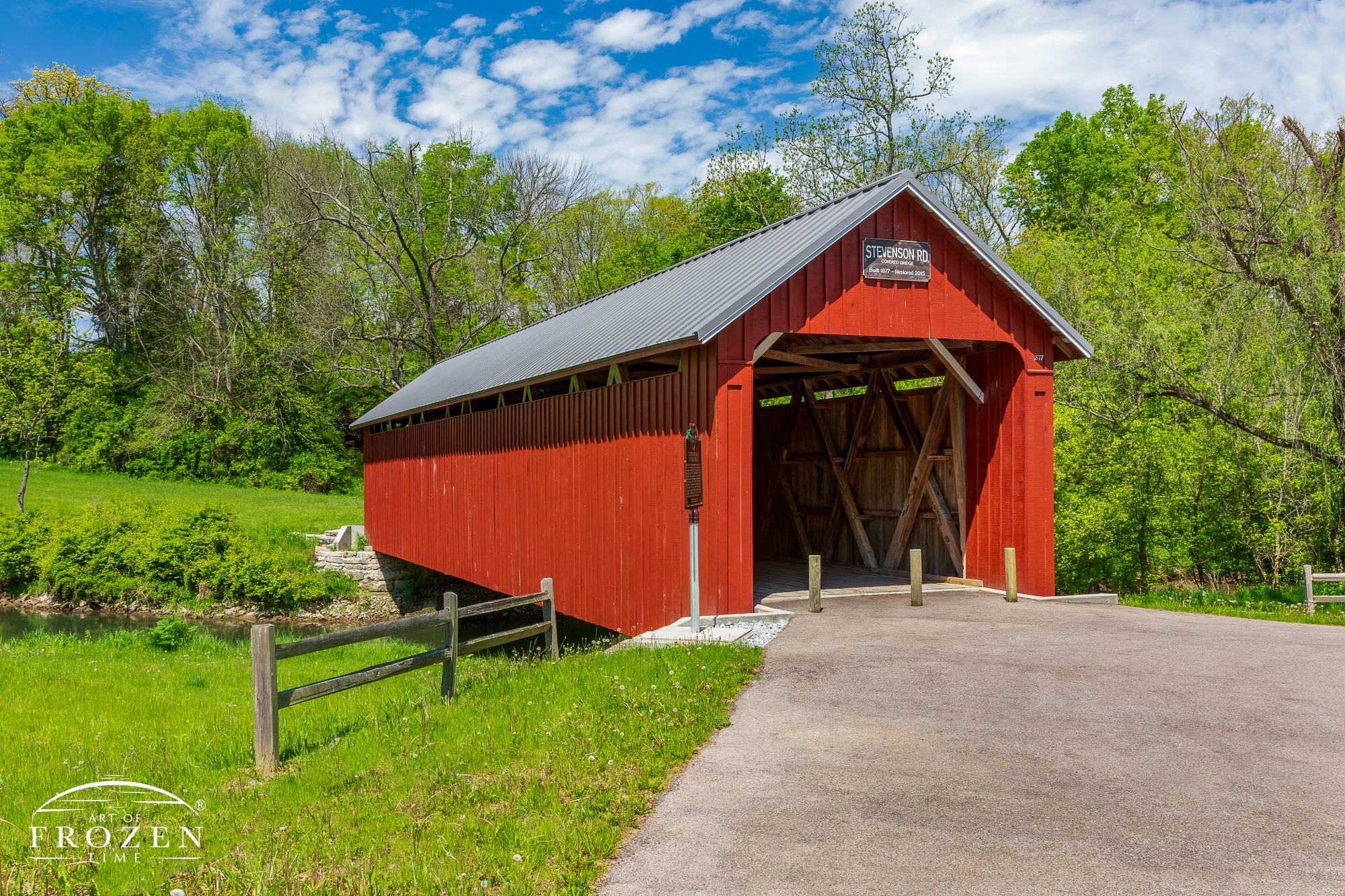 A covered bridge where its red paint contrasts with the green spring leaves and crystal blue skies