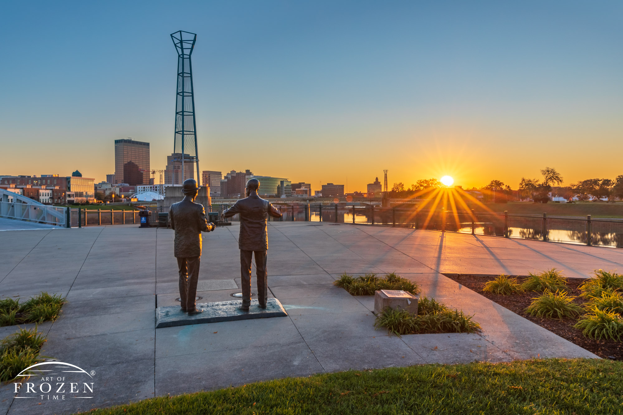 A statue of the Wright Brother looking west as the setting sun rakes light across the Dayton Skyline.