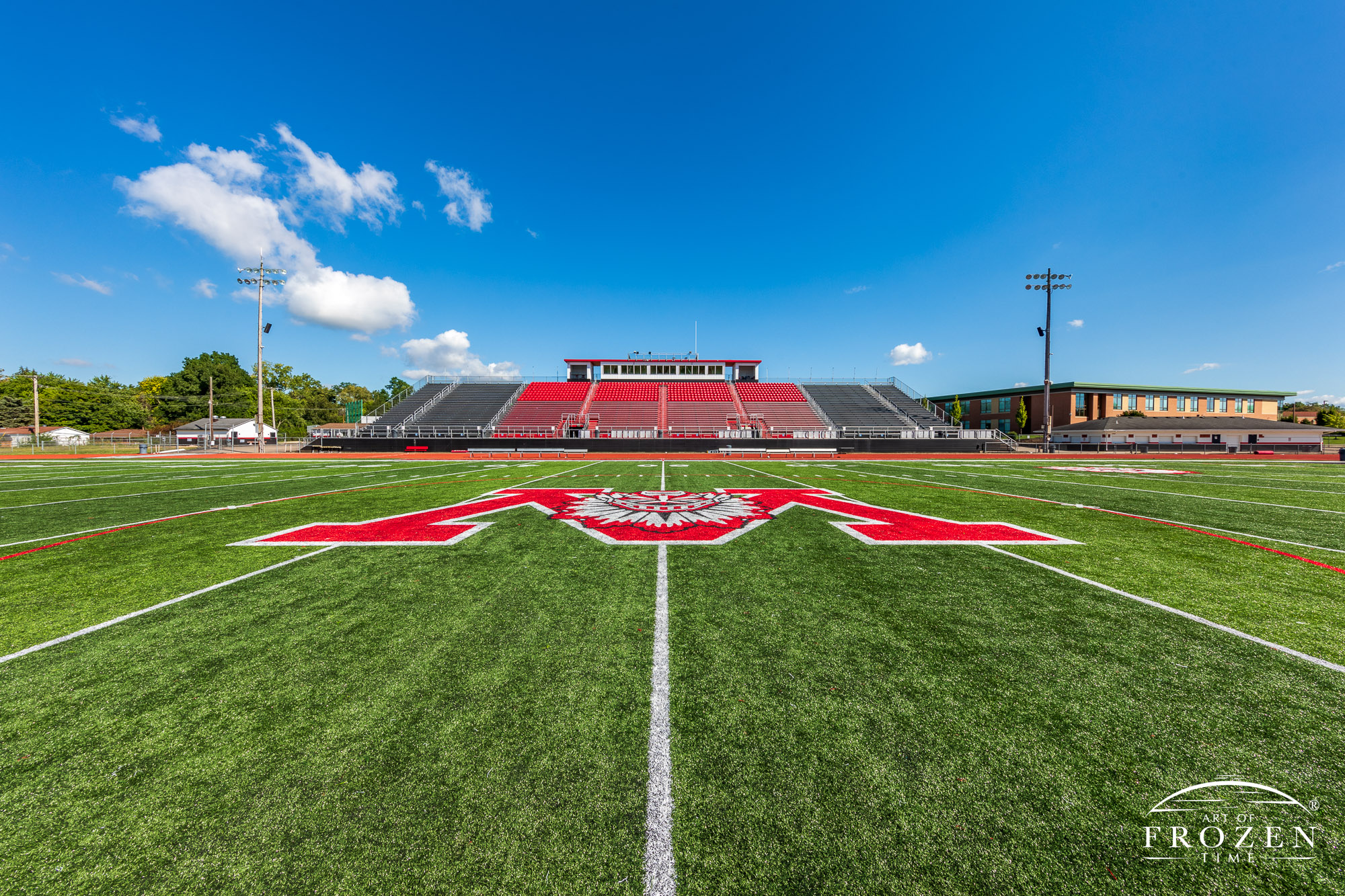 A view of Wayne High School’s Heidkamp Stadium in Huber Heights, Ohio featuring its Wayne Warrior Mascot spread across the 50-yard line under blue skies
