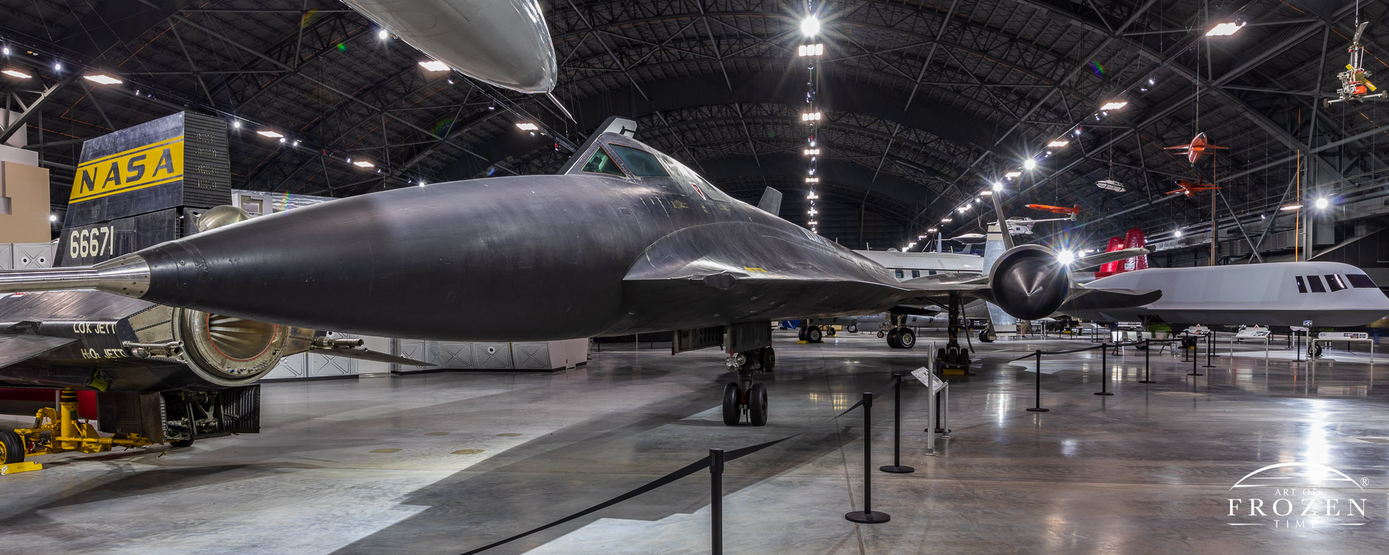 An image of the very long and black-painted YF-12 as it sits under the lights of the Air Force Museum along with other aerospace treasures.