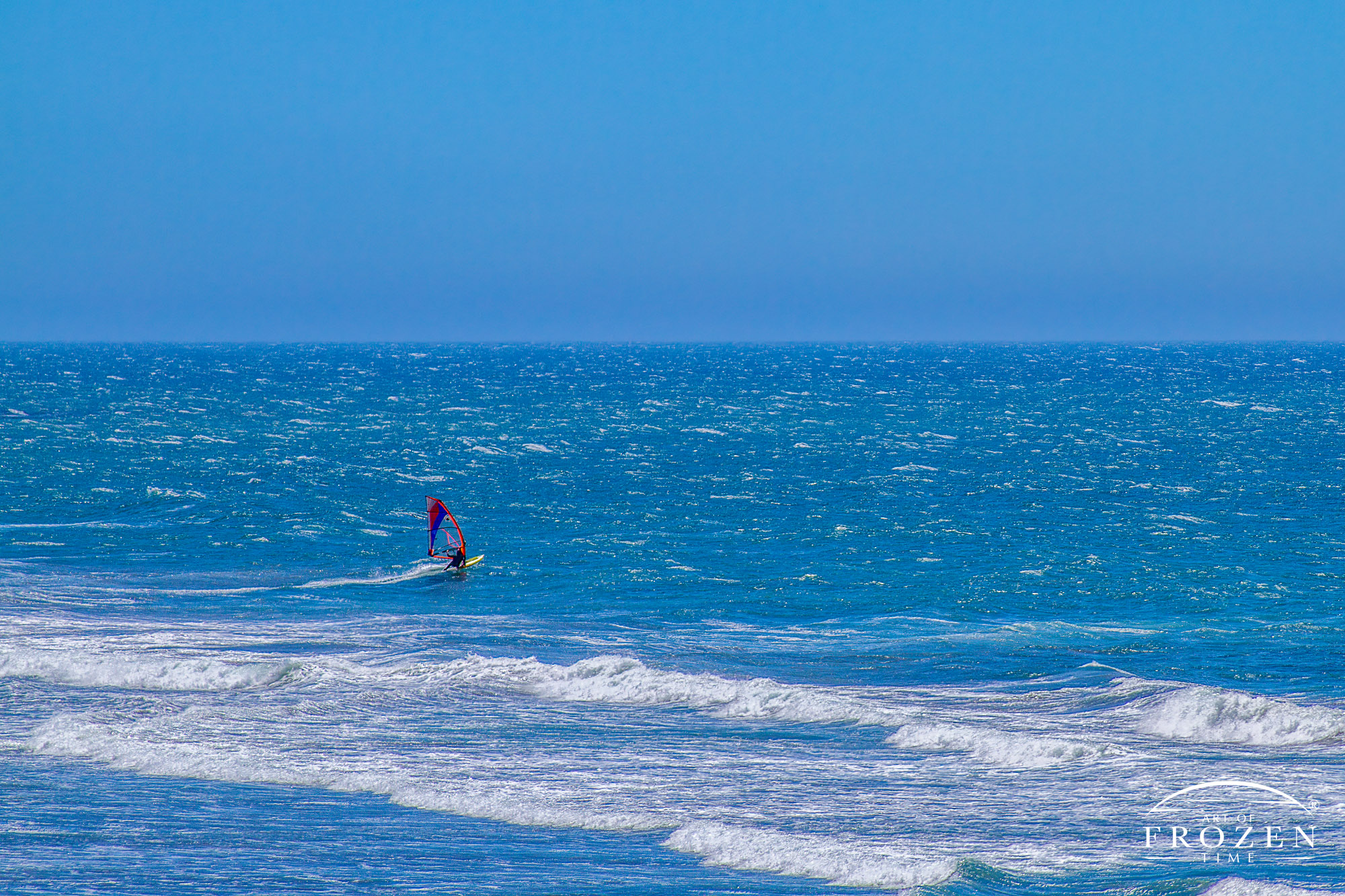 A windsurfer enjoying the blue ocean waters as the overhead sun makes the water sparkle