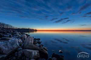 A deep twilight image as blue hour settles over Carlyle Lake where icy waves washed over shoreline rocks