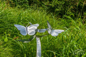 A sculpture of two aluminum butterflies with wings spread displayed near a small pond.
