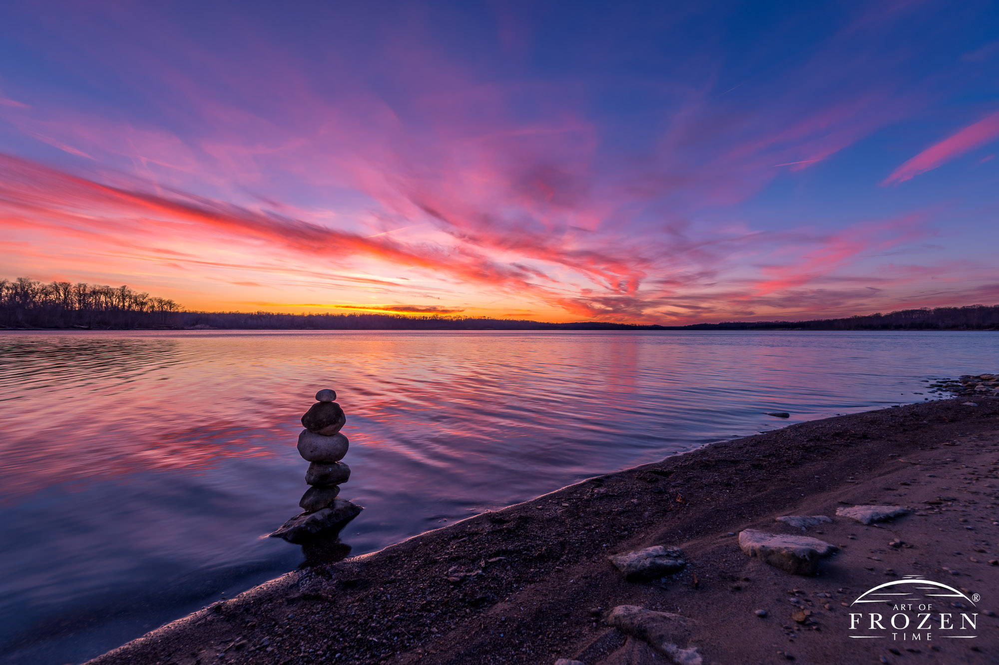 Peaceful twilight where calm waters of Caesar Creek reflects the colorful pink clouds as stacked rock cairn stands along the shoreline